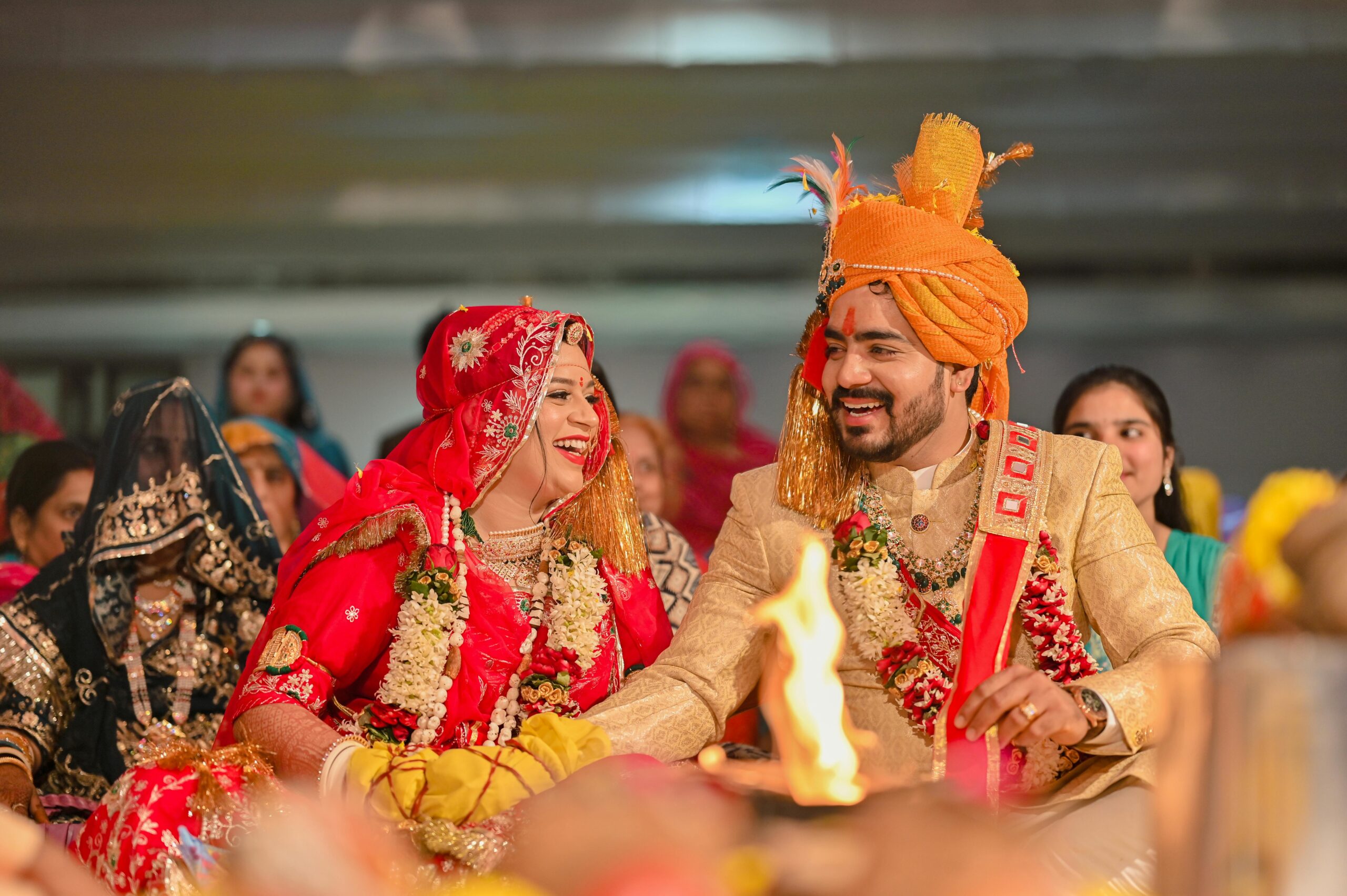 Traditional Indian wedding with smiling bride and groom in colorful attire surrounded by guests.
